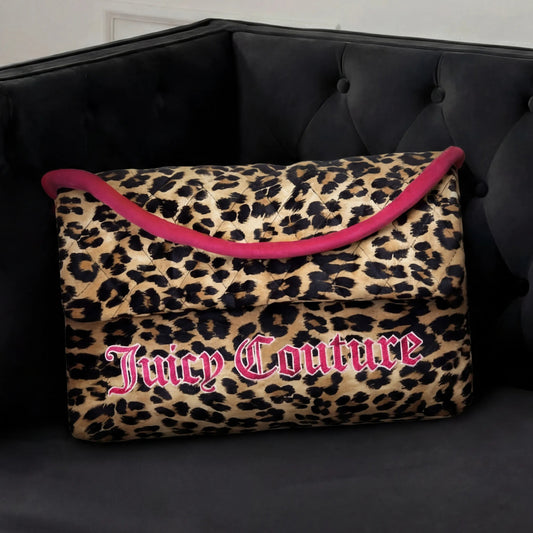 A Purse Decorative Pillow with leopard print, bold pink trim, and large Juicy Couture lettering sits on a tufted black velvet sofa, adding a trendy accent to any chic room.