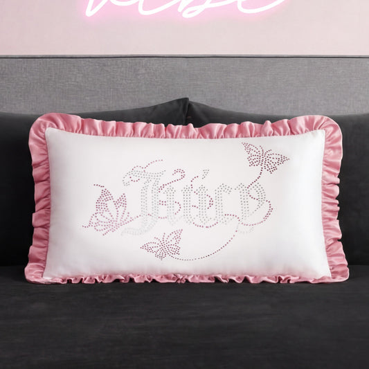 The Ruffle Decorative Pillow features pink ruffled edges, butterfly designs, and "fairy" in a decorative font on a pink and gray background with rhinestone accents, shown here on a dark sofa.