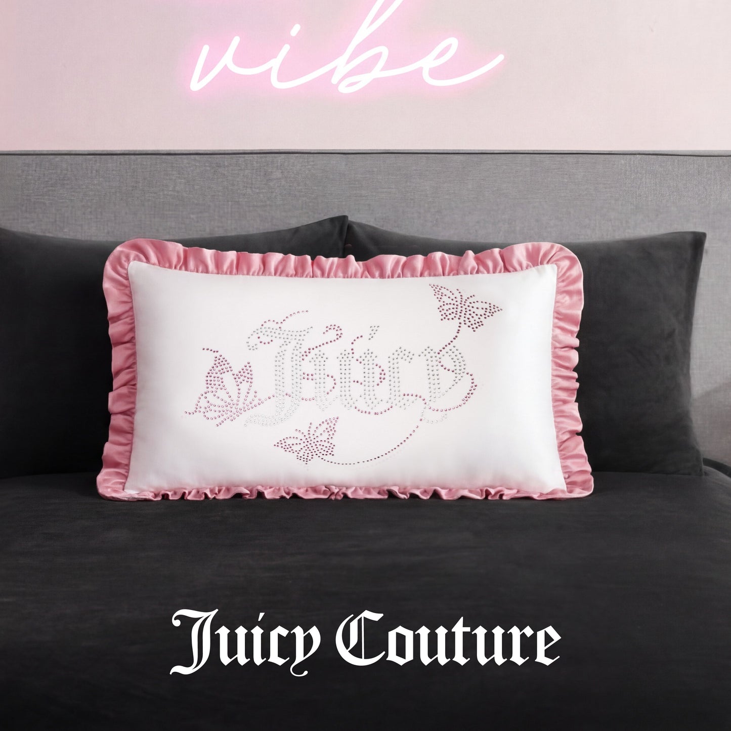 The Ruffle Decorative Pillow features white fabric, pink ruffled edges, and sparkling butterfly rhinestones, resting on a dark bed beneath a pink neon sign with Juicy Couture elegantly scripted at the bottom.