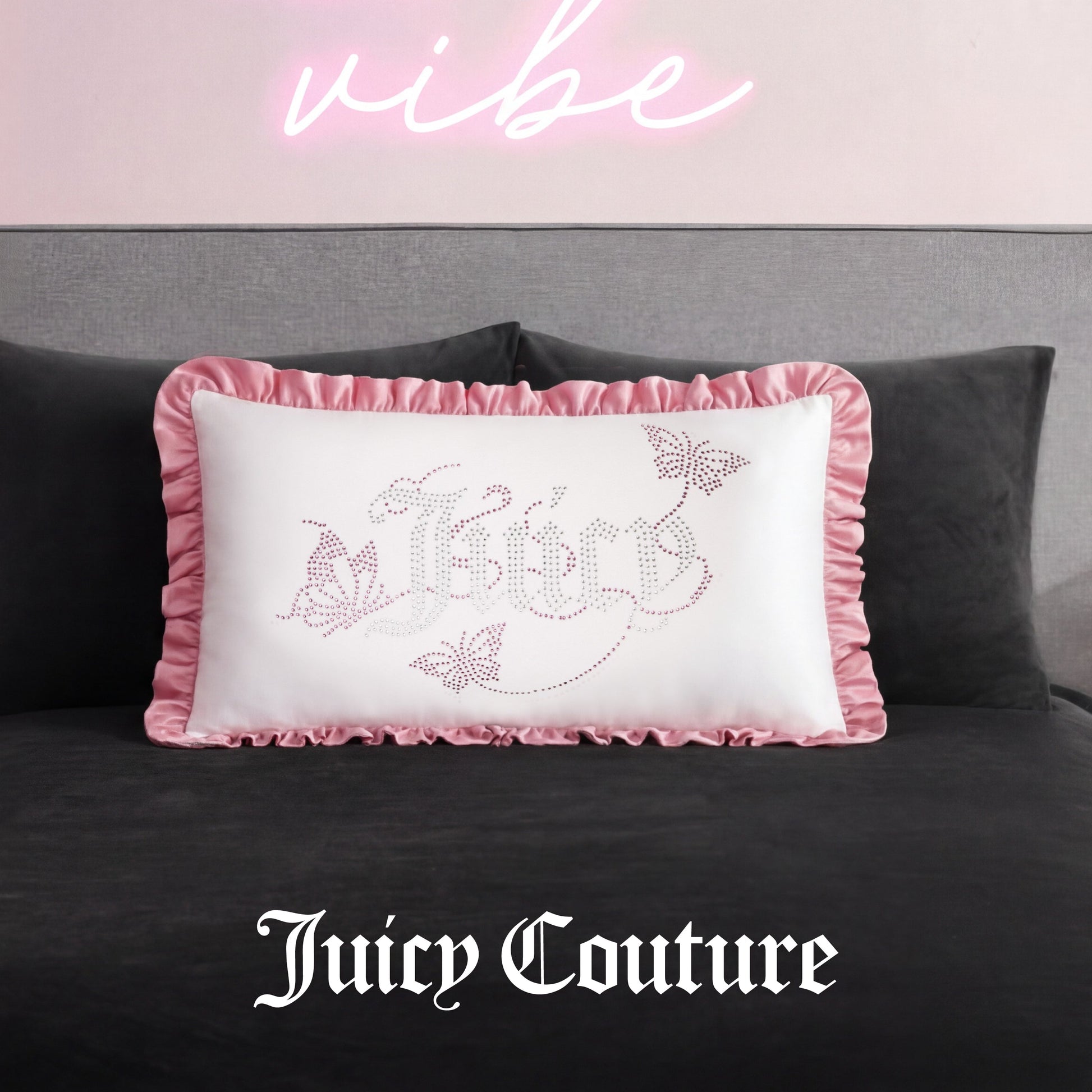 The Ruffle Decorative Pillow features white fabric, pink ruffled edges, and sparkling butterfly rhinestones, resting on a dark bed beneath a pink neon sign with Juicy Couture elegantly scripted at the bottom.