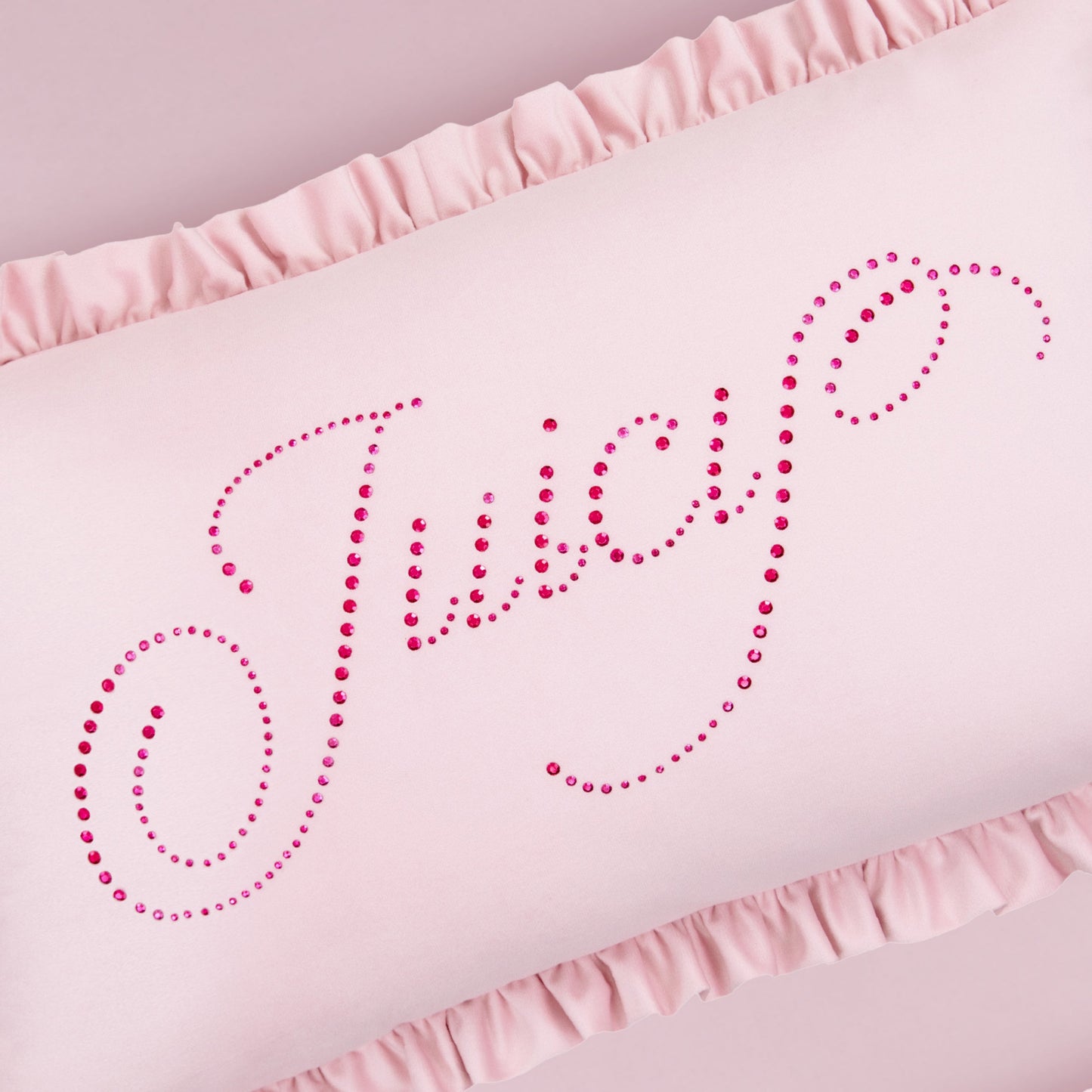 The Ruffle Decorative Pillow is light pink with ruffled edges and features "Juicy" in pink rhinestone cursive across the front.