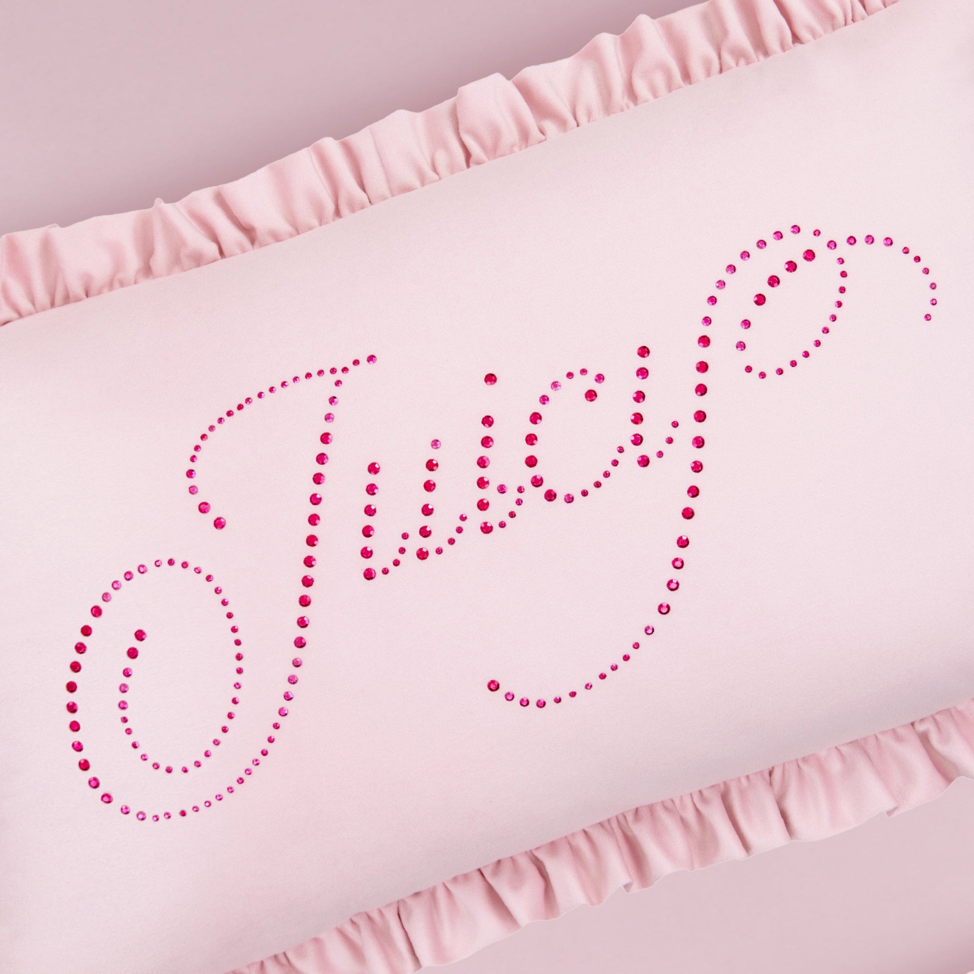 The Ruffle Decorative Pillow is light pink with ruffled edges and features "Juicy" in pink rhinestone cursive across the front.