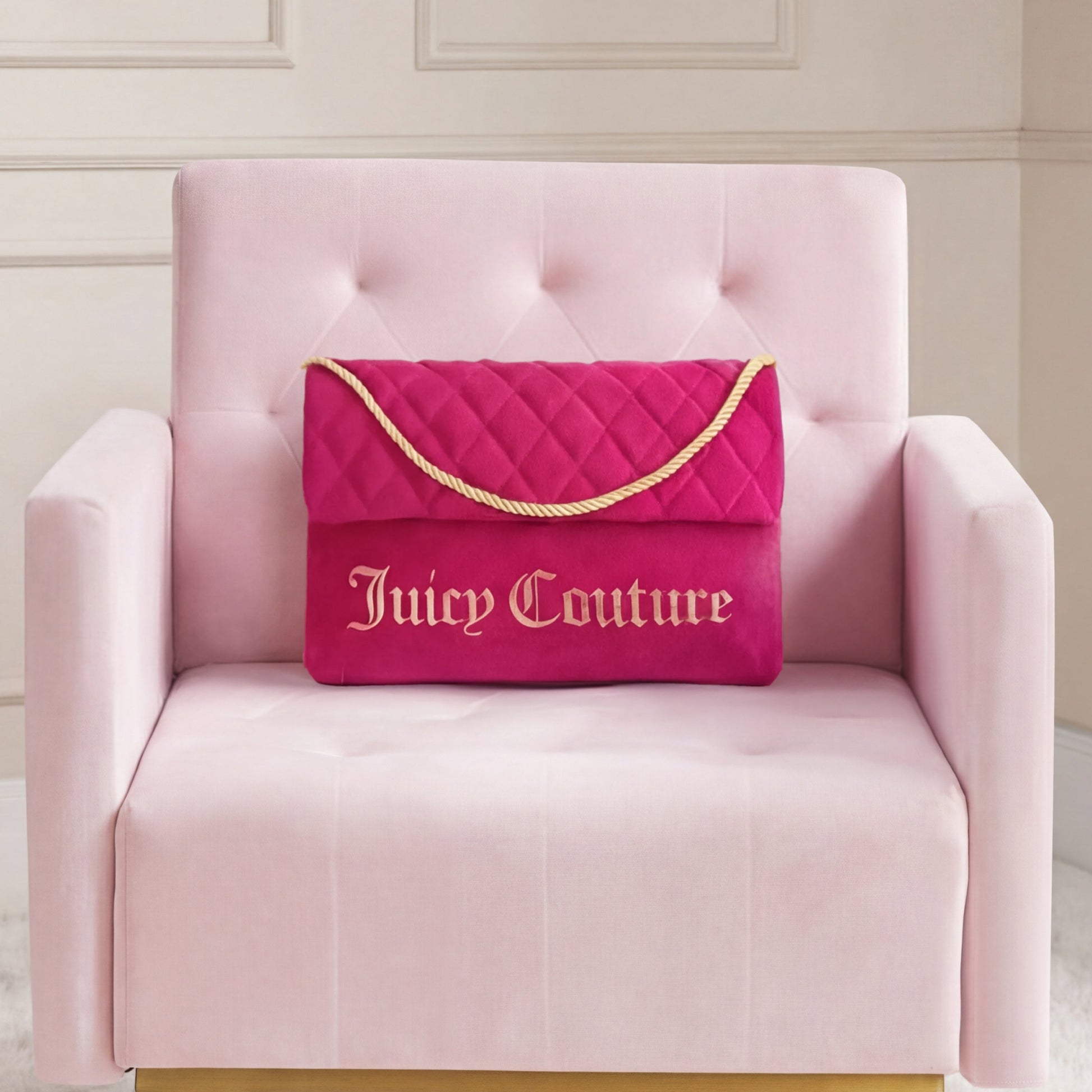 A Purse Decorative Pillow is paired with a bright pink Juicy Couture quilted bag on a pale pink armchair, set against a neutral paneled wall for a trendy accent.