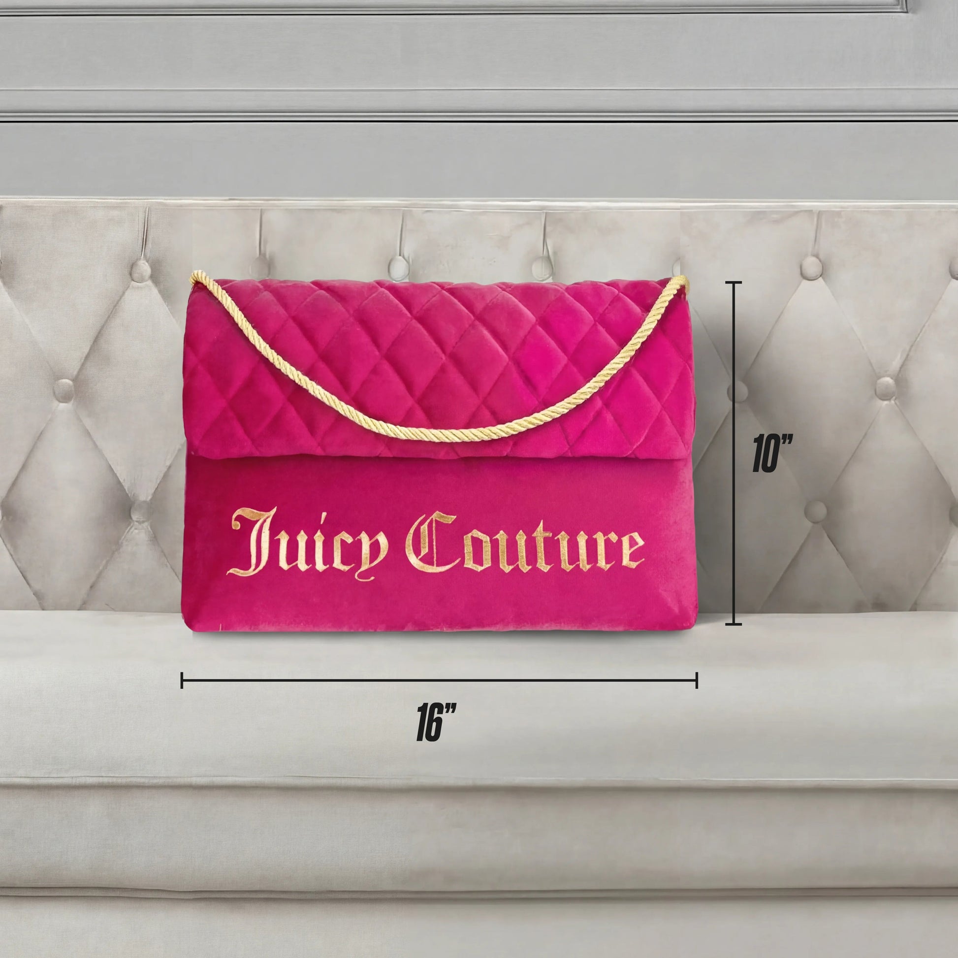 The Purse Decorative Pillow, in pink quilted fabric with gold lettering and a rope handle, measures 16" wide by 10" tall. Shown on a beige tufted couch, it adds a trendy accent to any space.