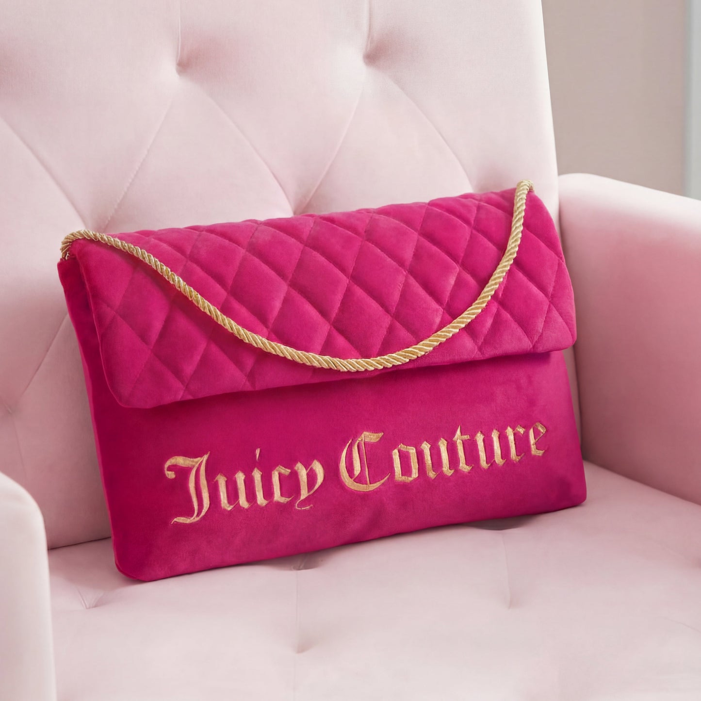 The Purse Decorative Pillow features bright pink quilting, gold embroidered lettering, and a gold rope strap—perfect as a stylish accent or clutch, displayed here on a pale pink velvet chair for a trendy touch to any room.