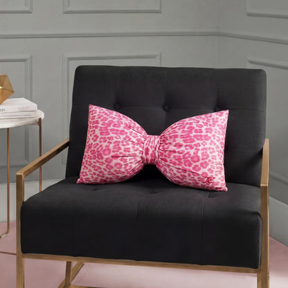 A black armchair with gold legs holds a large Bow Decorative Pillow in cheetah print. Next to it is a small side table topped with books and a gold geometric decor piece.