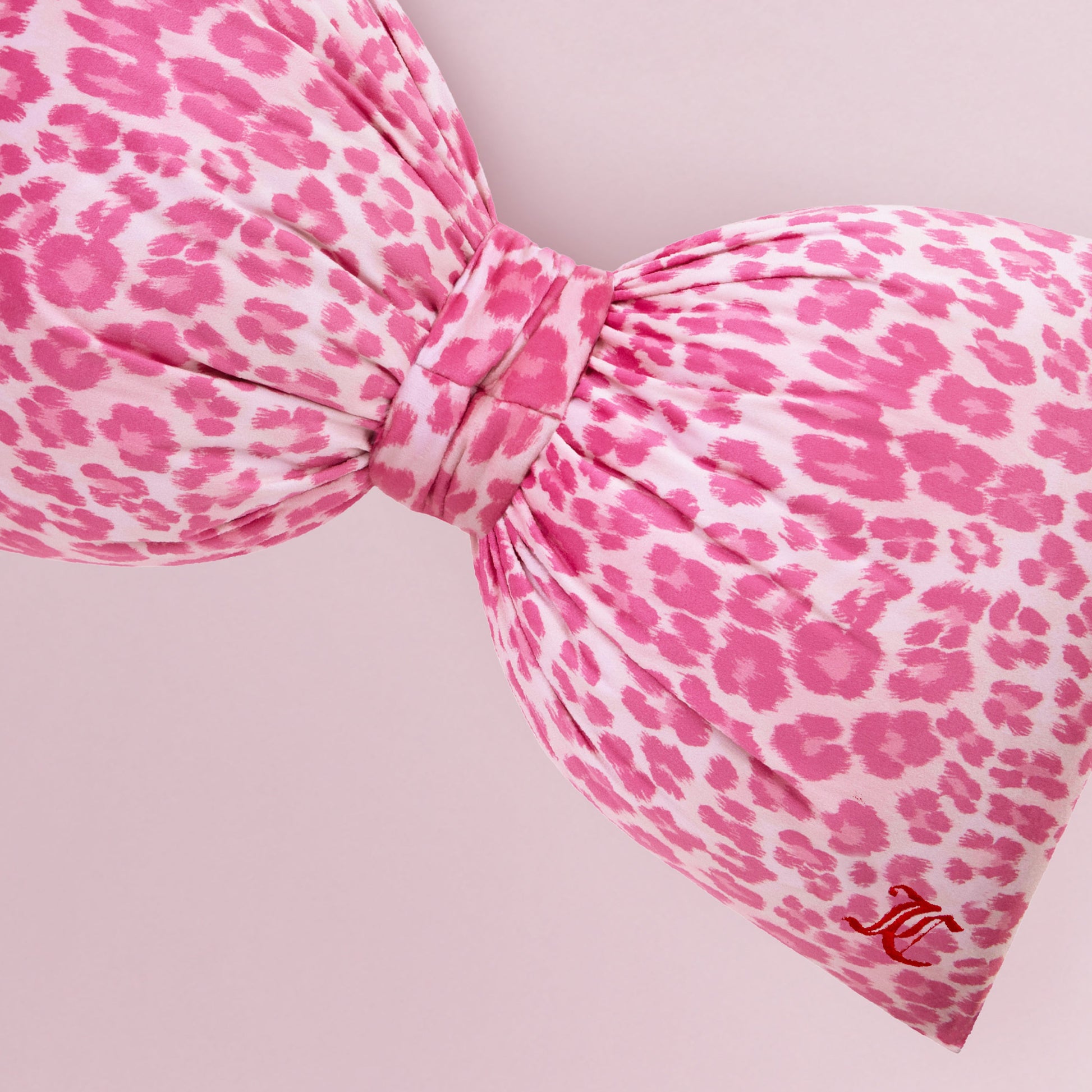 The Bow Decorative Pillow features a close-up of pink and white cheetah print fabric, a decorative bow, and a small red embroidered MC logo on the lower right side, set against a light pink background.