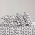 Four black and white butterfly patterned pillows from the Microfiber Sheet Set With Extra Pillowcases are stacked on a luxury bedspread—two upright and two flat—against a plain, light-colored wall.