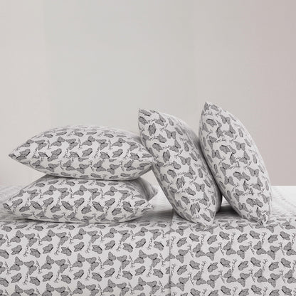 Four black and white butterfly patterned pillows from the Microfiber Sheet Set With Extra Pillowcases are stacked on a luxury bedspread—two upright and two flat—against a plain, light-colored wall.
