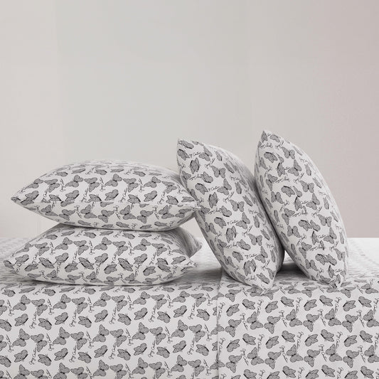 Four black and white butterfly patterned pillows from the Microfiber Sheet Set With Extra Pillowcases are stacked on a luxury bedspread—two upright and two flat—against a plain, light-colored wall.