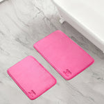Two quilted memory foam bath mats from the 2-piece set are placed on a light gray marble bathroom floor next to a white bathtub.
