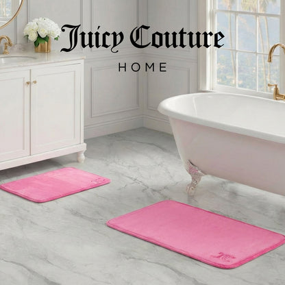 A luxurious bathroom with a white bathtub, marble floors, gold fixtures, and two pink Quilted Memory Foam Bath Mats. The Juicy Couture Home logo is displayed at the top of the image.