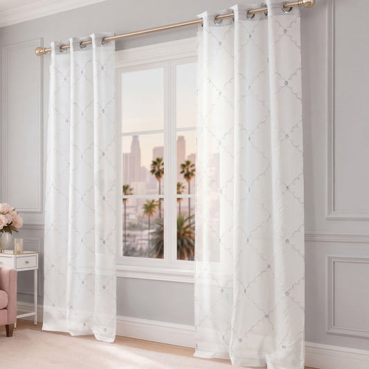 Scallop Diamond Sheer Window Curtains with a grommet header hang on a gold rod over a large window, revealing city buildings and palm trees outside. The room features gray walls, white trim, and elegant decor such as a pink chair and a vase of flowers.