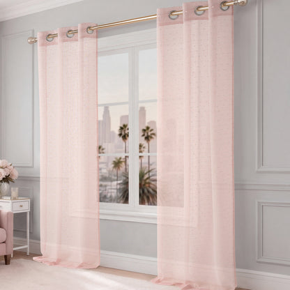 The Aurora Sheer Window Curtain in pink with a grommet header hangs from a gold rod, allowing natural light to fill the room. A cityscape with palm trees appears beyond the window, complementing the light gray walls and elegant decor.