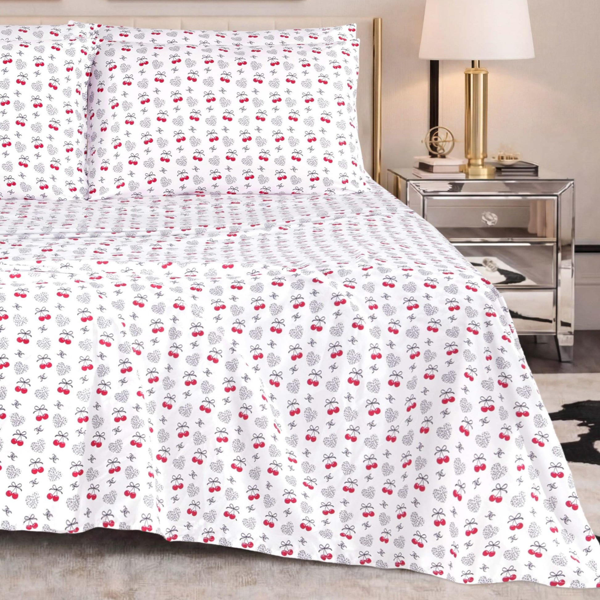 The Microfiber Sheet Set With Extra Pillowcases, featuring a subtle red and black cherry pattern, is paired with a mirrored nightstand topped with a lamp and decorative accents to create a modern bedroom setting enhanced by luxury bedding for superior comfort and style.
