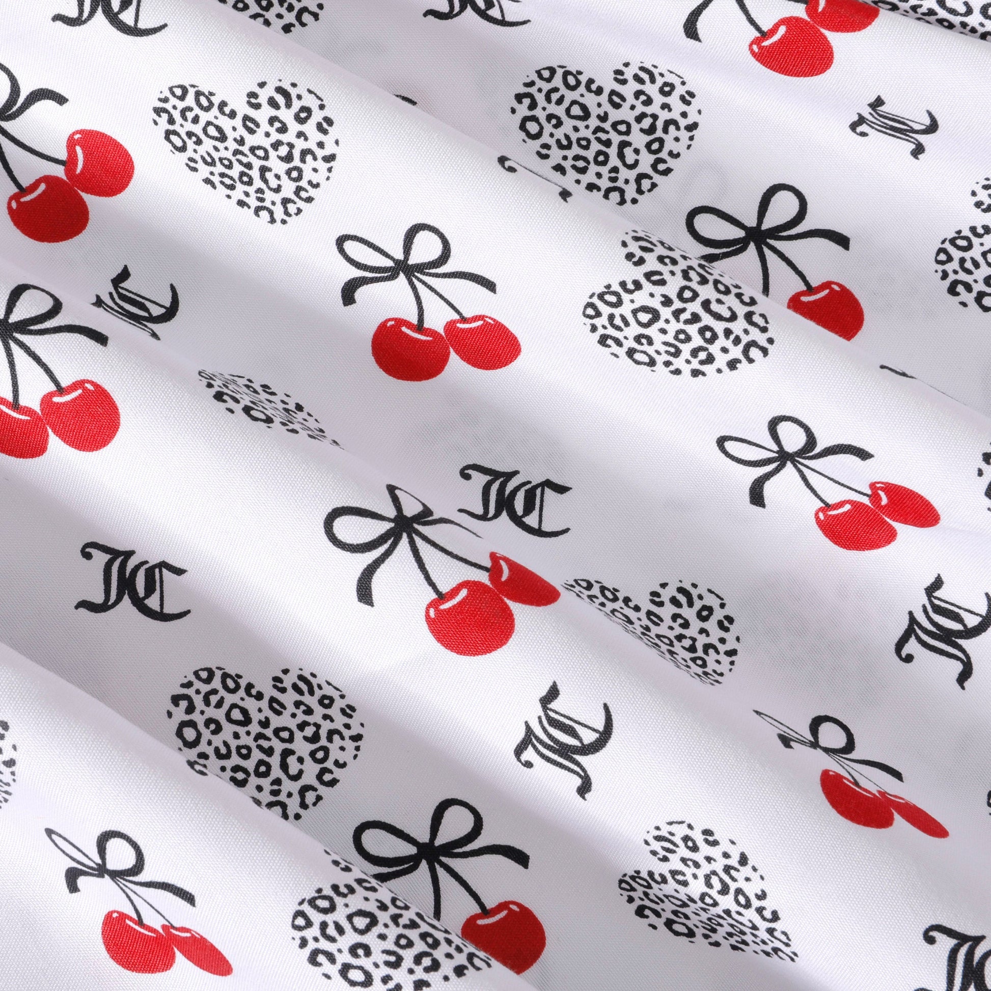 White microfiber fabric featuring a repeating pattern of red cherries, black bows, leopard print hearts, and black letter initials. The smooth, slightly shiny background embodies the signature playful elegance of a Juicy Couture Microfiber Sheet Set With Extra Pillowcases. This luxury bedding adds a bold touch of style to any bedroom décor.
