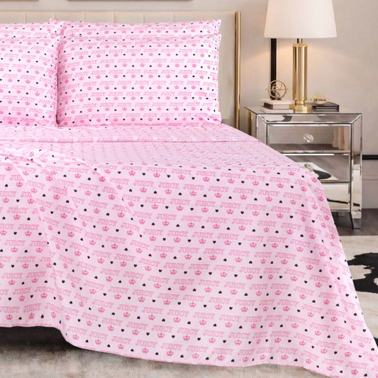 The pink bedspread and pillows showcase repeating JUICY text with heart and lips patterns, perfectly capturing the playful essence of Juicy Couture bedding. The bed is complemented by the Microfiber Sheet Set With Extra Pillowcases, adding an ultra-soft touch. A mirrored nightstand with a lamp and décor completes the modern bedroom setting.