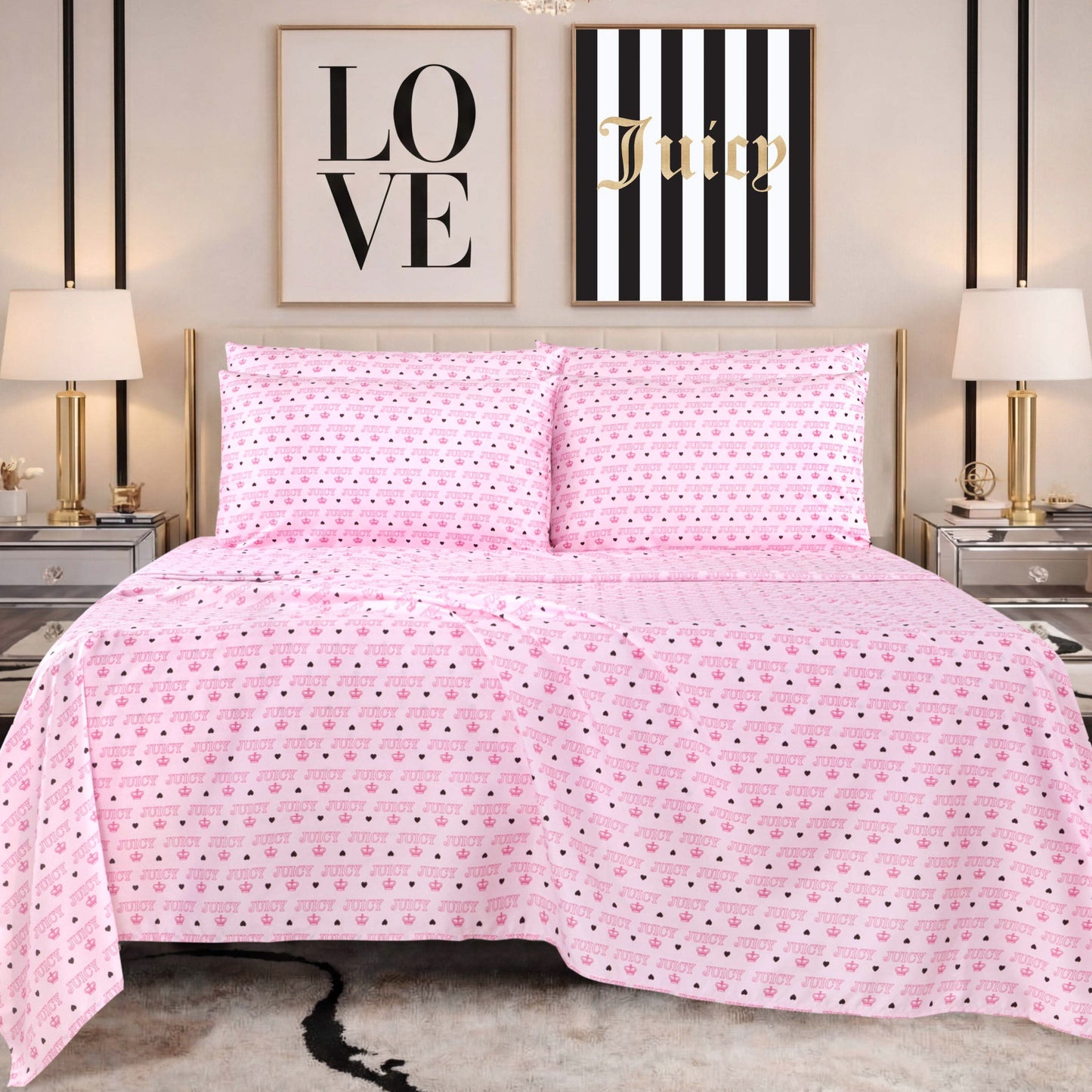 A bed with pink heart-patterned Juicy Couture bedding and a Microfiber Sheet Set With Extra Pillowcases sits between two mirrored nightstands with lamps. Behind the bed are two framed wall art pieces, one reading LOVE and the other Juicy on a striped background.