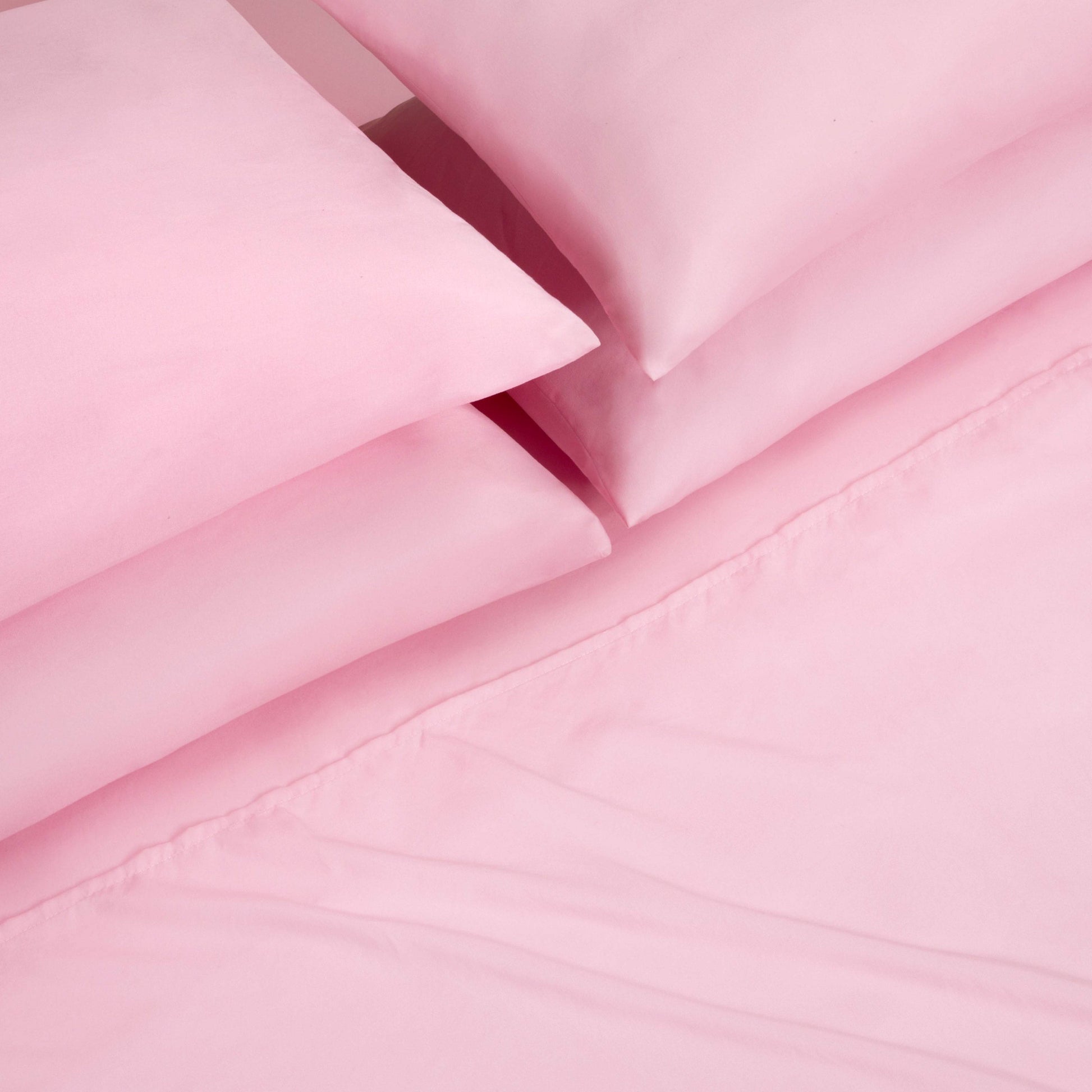 A close-up view of a neatly folded Microfiber Sheet Set With Extra Pillowcases, featuring pink bed sheets and pillowcases arranged on a matching pink bedspread, showcasing the essence of luxury bedding.