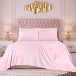 A neatly made bed with a light pink Microfiber Sheet Set With Extra Pillowcases is flanked by two gold lamps on white nightstands and sits against a tufted beige headboard. A gold abstract wall art piece hangs above the bed, while the soft, neutral decor throughout the room lends a touch of luxury bedding elegance.