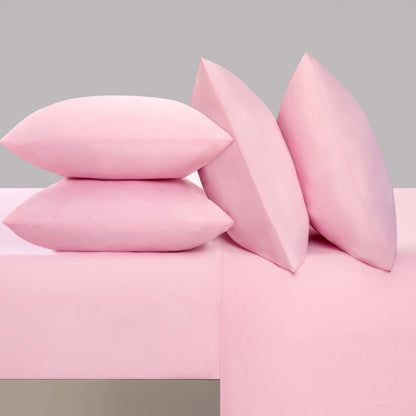 Four light pink pillows are arranged on the Microfiber Sheet Set With Extra Pillowcases, with two pillows stacked flat on the left and two pillows standing upright on the right against a simple gray background. This luxury bedding ensemble adds a touch of softness and sophistication to any room.