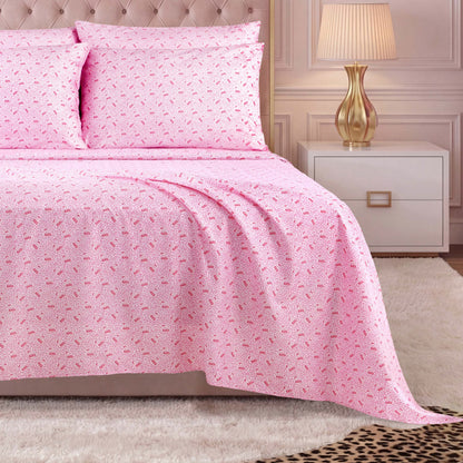 A neatly made bed with a Microfiber Sheet Set With Extra Pillowcases in pink patterns and coordinating pillows sits beside a gold lamp on a white nightstand, all atop a beige carpet with a small animal print rug—perfect for those who appreciate luxury bedding.