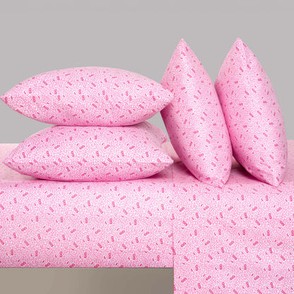 Four pink pillows with a small, repeating pattern are stacked and propped up on a matching Microfiber Sheet Set With Extra Pillowcases, all set against a plain light gray background for a touch of luxury bedding perfection.