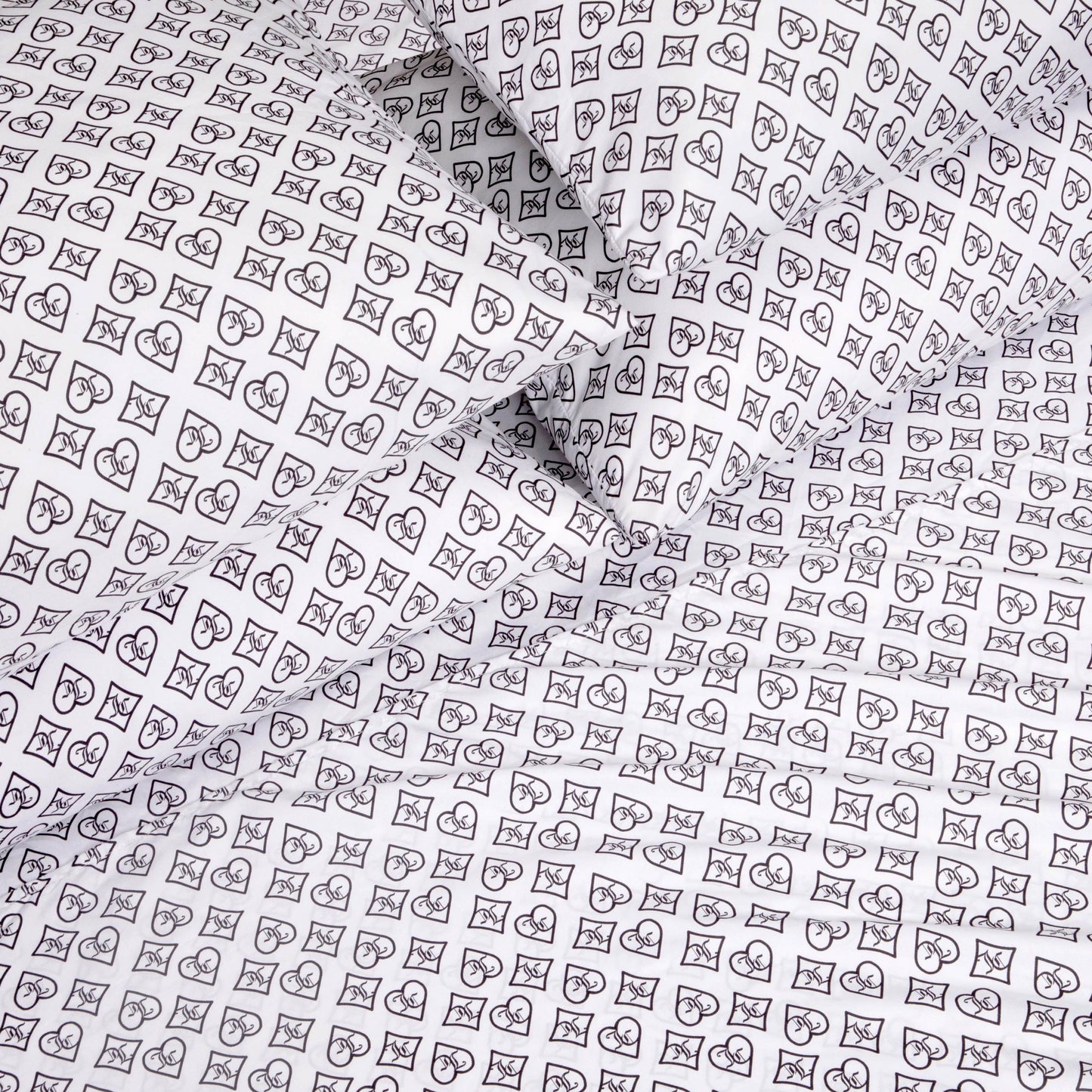 The Microfiber Sheet Set With Extra Pillowcases showcases white luxury bedding adorned with a black outlined pattern of hearts, crescent moons, and stars arranged in small square grids, elegantly covering multiple pillows and sheets.