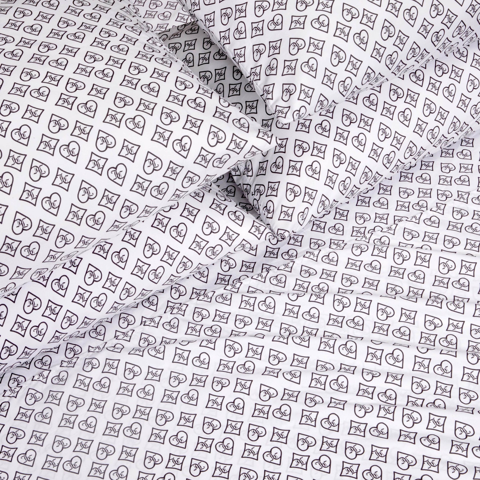 The Microfiber Sheet Set With Extra Pillowcases showcases white luxury bedding adorned with a black outlined pattern of hearts, crescent moons, and stars arranged in small square grids, elegantly covering multiple pillows and sheets.