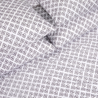 The Microfiber Sheet Set With Extra Pillowcases showcases white luxury bedding adorned with a black outlined pattern of hearts, crescent moons, and stars arranged in small square grids, elegantly covering multiple pillows and sheets.