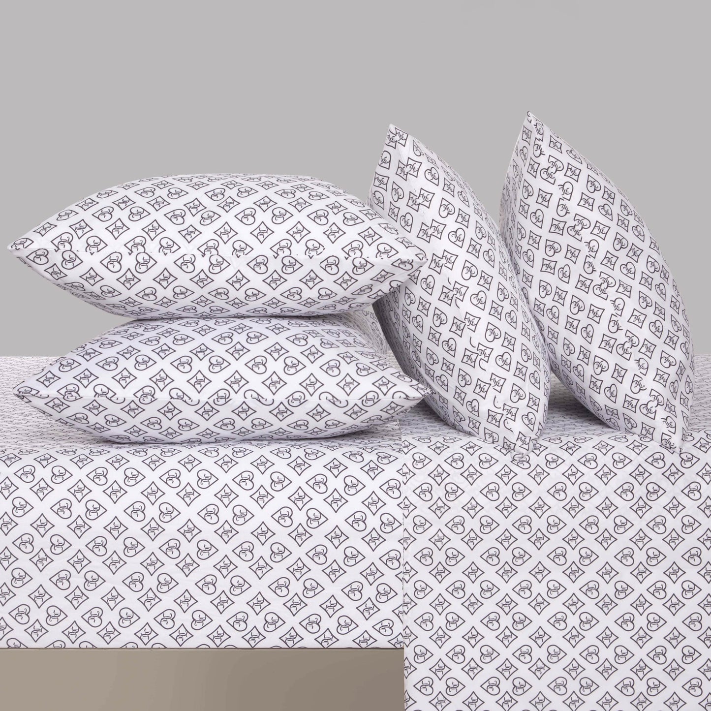 Four white pillows and a bedspread with a repeating black geometric pattern are arranged on a neatly made bed against a plain gray background, highlighting the sophistication of the Microfiber Sheet Set With Extra Pillowcases.