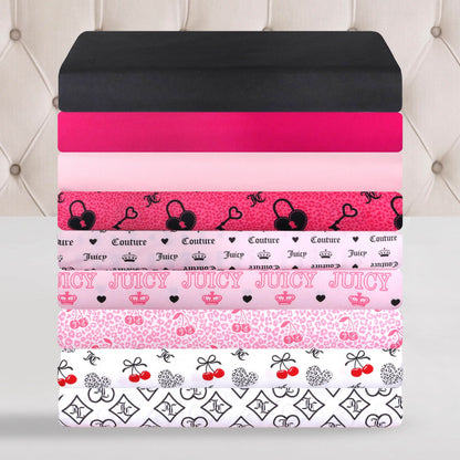 A neatly stacked pile of folded bedsheets in various pink, black, and white patterns—including hearts, crowns, bows, animal prints, and the repeated word “Juicy”—showcases the stylish Microfiber Sheet Set With Extra Pillowcases by Juicy Couture, perfect for adding a touch of luxury to your bedding.