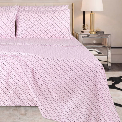 A neatly made bed with a pale pink Microfiber Sheet Set With Extra Pillowcases, featuring a small repeating black pattern, is situated next to a mirrored nightstand with a gold lamp and books in a modern bedroom setting.