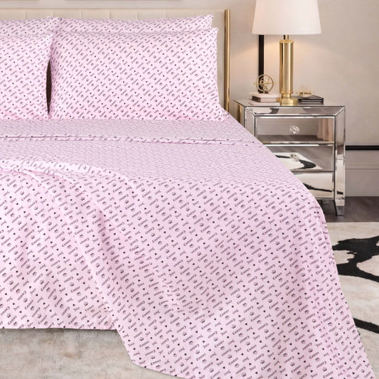 A neatly made bed with a pale pink Microfiber Sheet Set With Extra Pillowcases, featuring a small repeating black pattern, is situated next to a mirrored nightstand with a gold lamp and books in a modern bedroom setting.