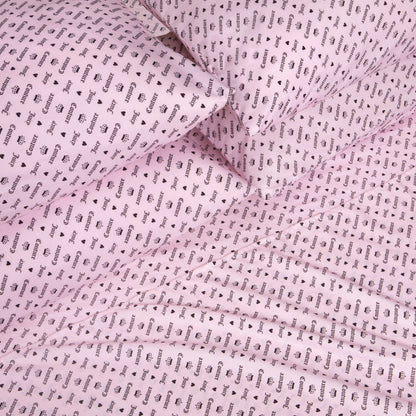 The Microfiber Sheet Set With Extra Pillowcases, featuring pink bed sheets and pillowcases adorned with a repeating black “Gucci” wordmark and logo pattern, is neatly arranged to create an eye-catching, luxurious look for any bedroom. This set delivers a fashionable flair that rivals the chic style of a Juicy Couture sheet set.