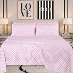 A neatly made bed with pink patterned bedding, featuring a Microfiber Sheet Set With Extra Pillowcases for added style, is flanked by two lamps on mirrored nightstands. Above the bed are two wall art pieces: one says LOVE and the other says Juicy on black and white stripes.