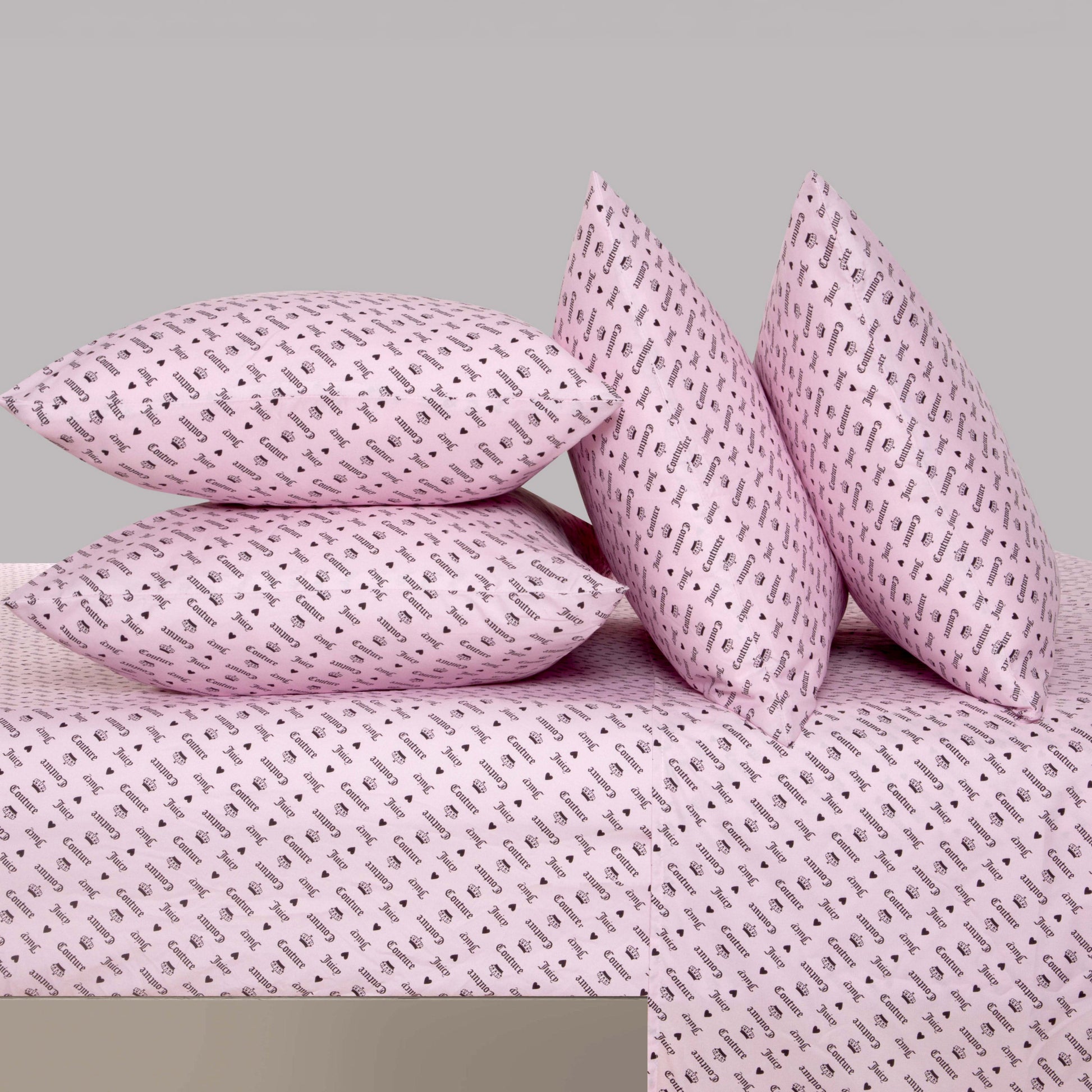 Four pink pillows with small black musical note patterns are arranged on the Microfiber Sheet Set With Extra Pillowcases in a matching pink tone, featuring the same playful design. This luxury bedding creates a stylish contrast against the plain gray background.