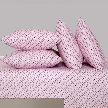 Four pink pillows with small black musical note patterns are arranged on the Microfiber Sheet Set With Extra Pillowcases in a matching pink tone, featuring the same playful design. This luxury bedding creates a stylish contrast against the plain gray background.