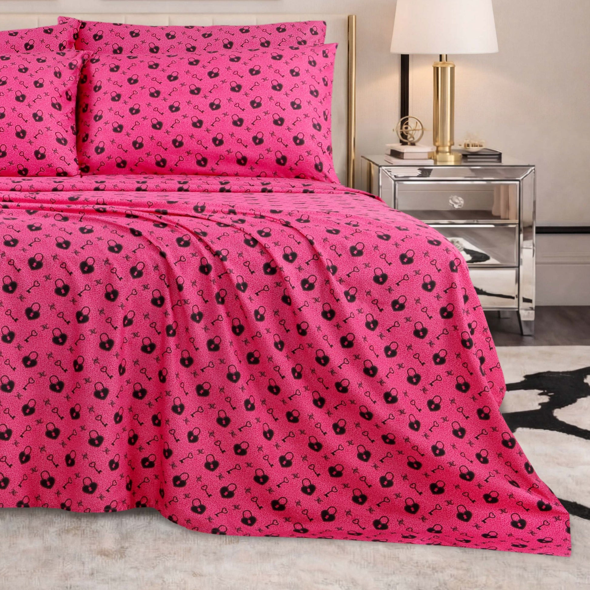 A neatly made bed with the Microfiber Sheet Set With Extra Pillowcases in bright pink featuring a floral pattern, two matching pillows, a mirrored nightstand with a lamp, and a modern rug in a stylish bedroom.