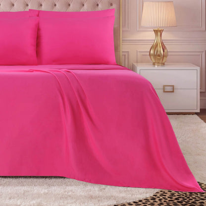 A neatly made bed with a bright pink Microfiber Sheet Set With Extra Pillowcases, next to a white nightstand with a gold lamp, on a light-colored shaggy rug in a softly lit room.