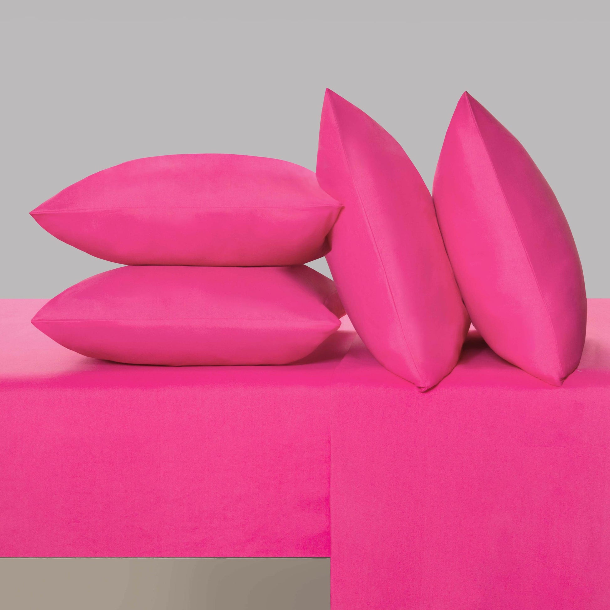 Four bright pink pillows from the Microfiber Sheet Set With Extra Pillowcases are arranged on a matching pink surface and background. Two pillows are stacked horizontally while two stand upright, leaning stylishly against the stack—creating a chic look reminiscent of luxury bedding or a bold designer accent.