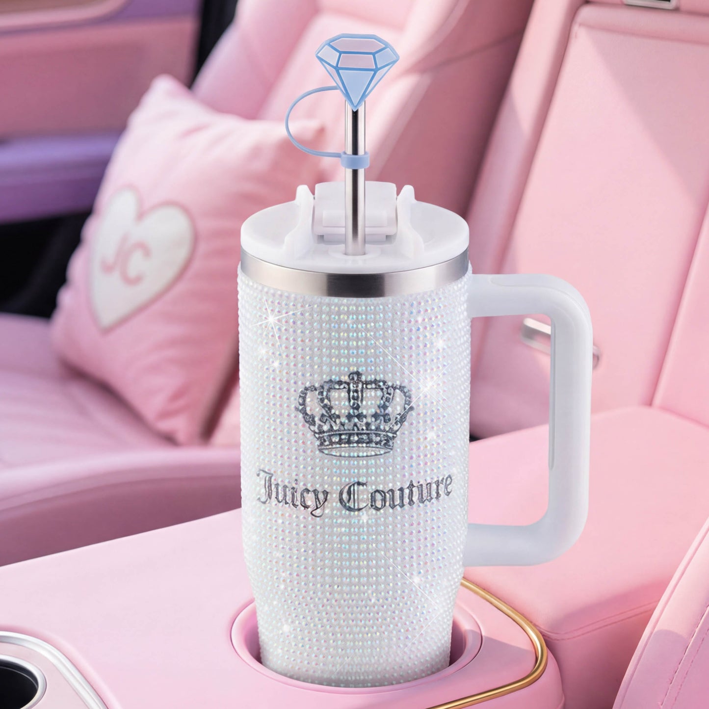 A Diamond Bling Stainless Steel Tumbler with Handle and Straw, 30 oz, featuring a sparkling crown logo, sits in a pink car interior. This decorative tumbler includes a large handle and a straw topped with an eye-catching diamond-shaped accent.