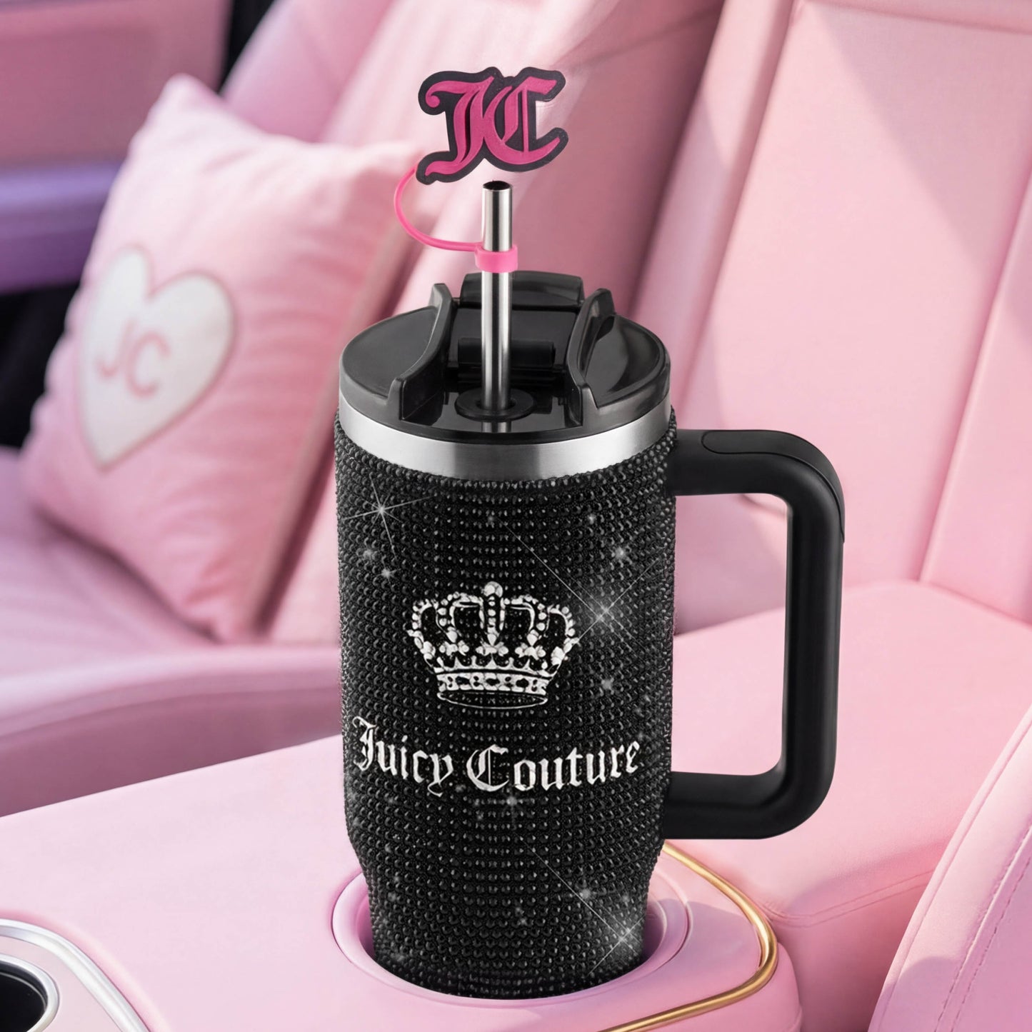 A Diamond Bling Stainless Steel Tumbler with Handle and Straw, 30 oz, covered in sparkling rhinestones, is placed in a pink car cup holder. The straw is adorned with a pink Juicy Couture logo charm, while a heart-shaped JC cushion on the seat completes the glamorous look of this dazzling tumbler accessory.