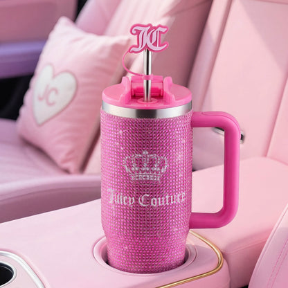 A Diamond Bling Stainless Steel Tumbler with Handle and Straw, 30 oz, in sparkling pink sits in a pink car interior. The tumbler features rhinestone accents, a crown logo, prominent “Juicy Couture” text, and a JC logo straw topper.