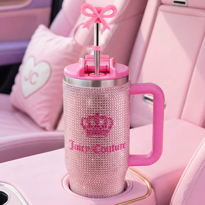 A Diamond Bling Stainless Steel Tumbler with Handle and Straw, 30 oz, adorned with jeweled accents and a bow-shaped straw, sits in the cup holder of a pink car with matching pink seats and a heart-shaped pillow embroidered with JC.