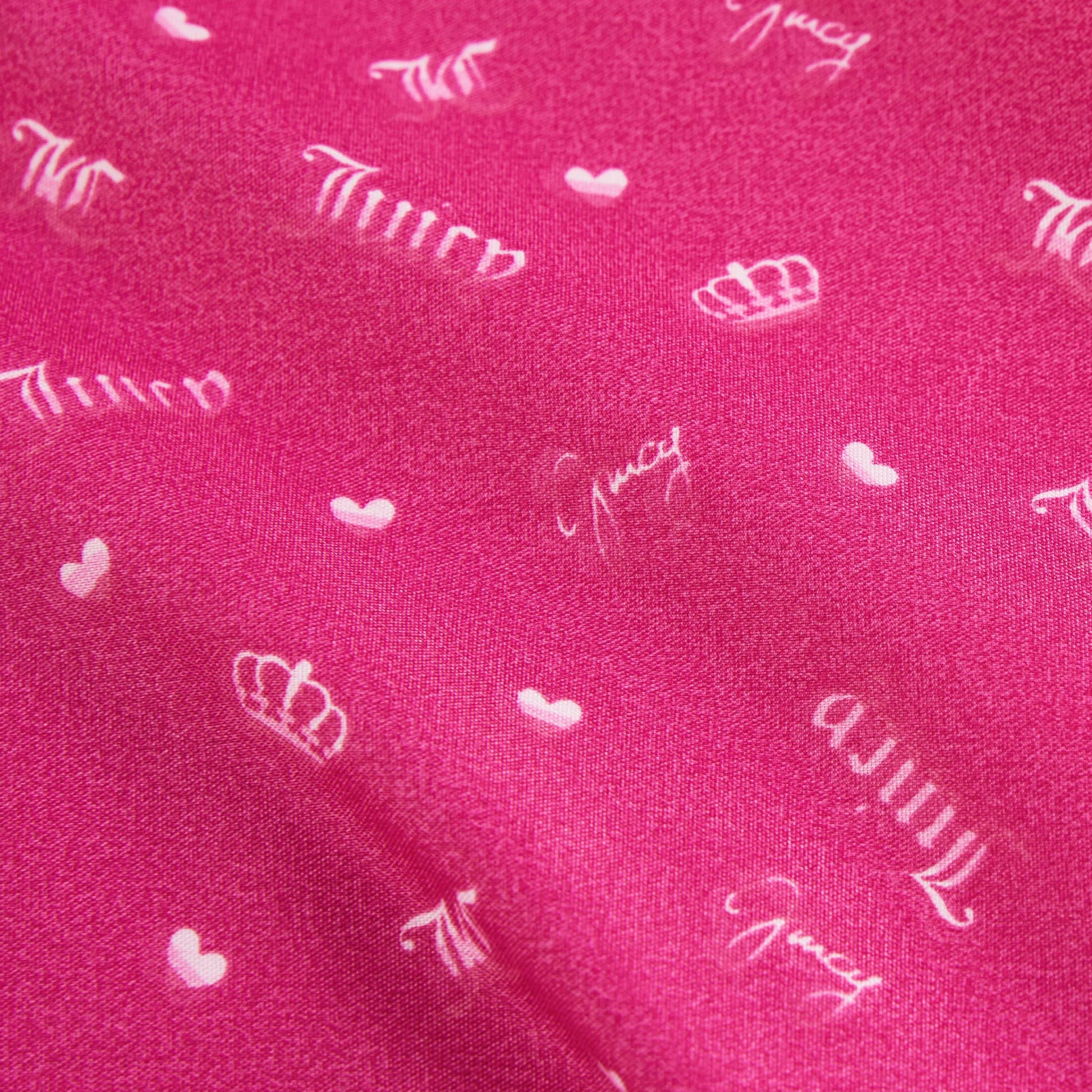 The Microfiber Sheet Set With Extra Pillowcases features bright pink bedding with white crowns, small hearts, and "Juicy" in cursive, adding a stylish and cozy touch to any room.