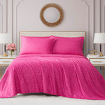 A neatly made bed features the Microfiber Sheet Set With Extra Pillowcases in bright pink, plus matching pillows with small white patterns. The room includes a round gold mirror, white lamps, and pink flowers on bedside tables.