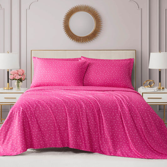 A neatly made bed features the Microfiber Sheet Set With Extra Pillowcases in bright pink, plus matching pillows with small white patterns. The room includes a round gold mirror, white lamps, and pink flowers on bedside tables.