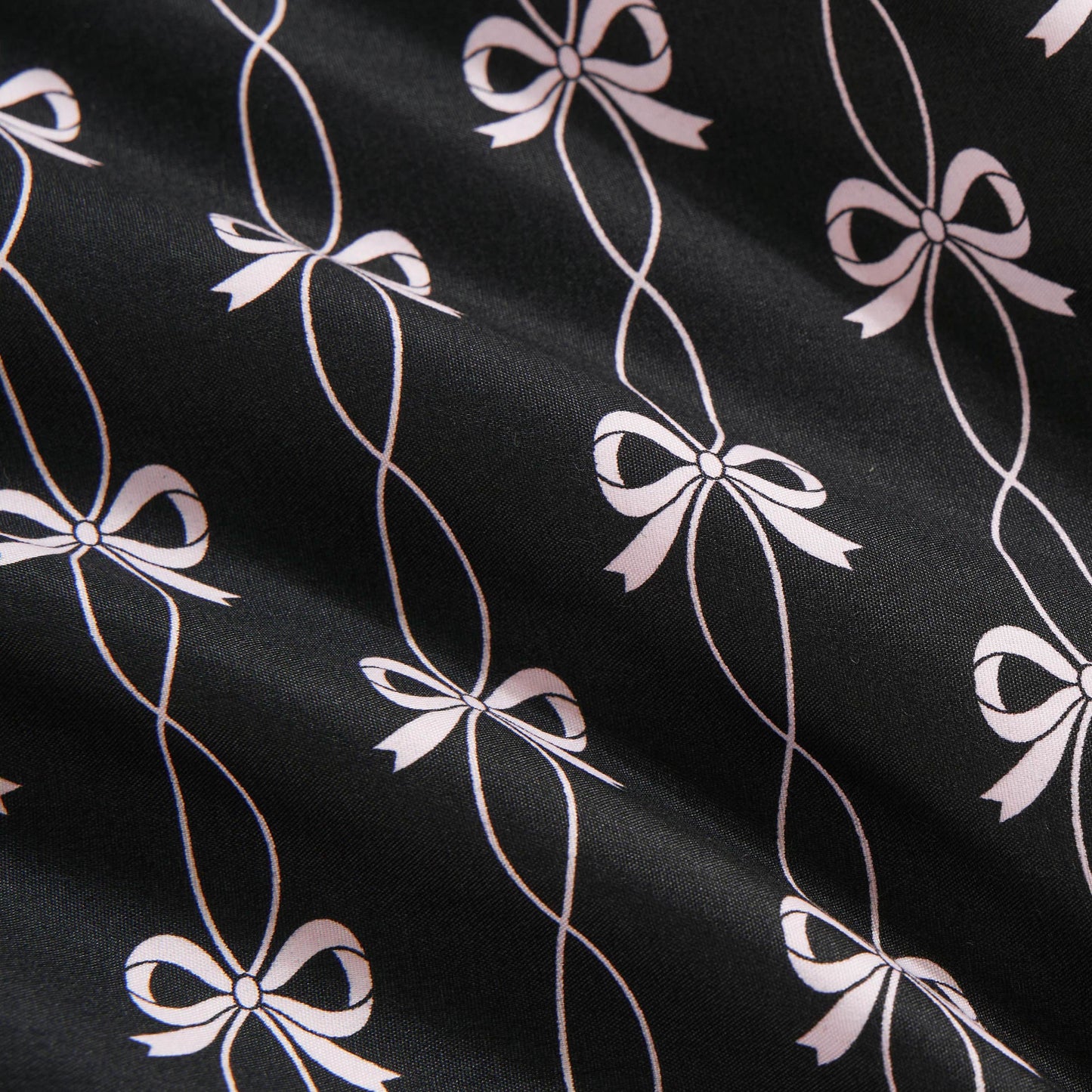 The Microfiber Sheet Set With Extra Pillowcases features black sheets with a white, stylized bow pattern connected by looping lines. The slightly textured surface and soft folds add a luxurious touch to any bedroom.