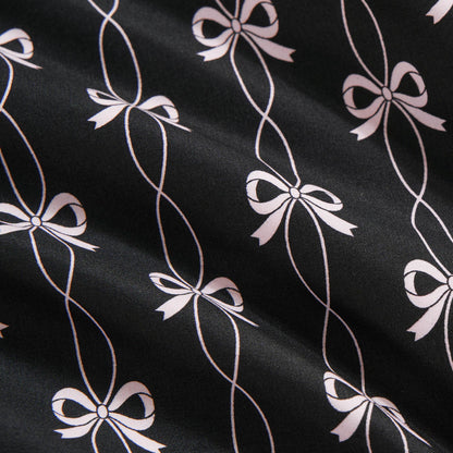 The Microfiber Sheet Set With Extra Pillowcases features black sheets with a white, stylized bow pattern connected by looping lines. The slightly textured surface and soft folds add a luxurious touch to any bedroom.